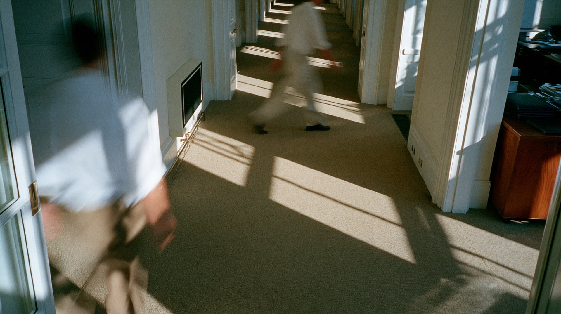 Two people walking through a sunlit office corridor, blurred in motion