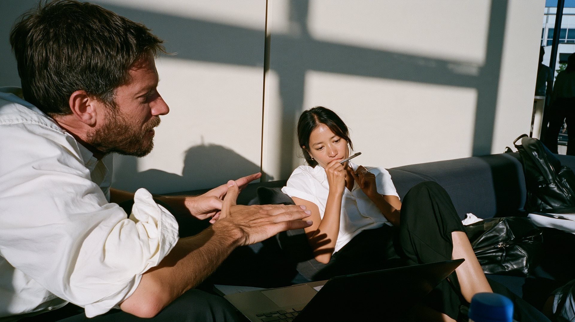 Two people in conversation on a sofa, one explaining with his hands, the other listening