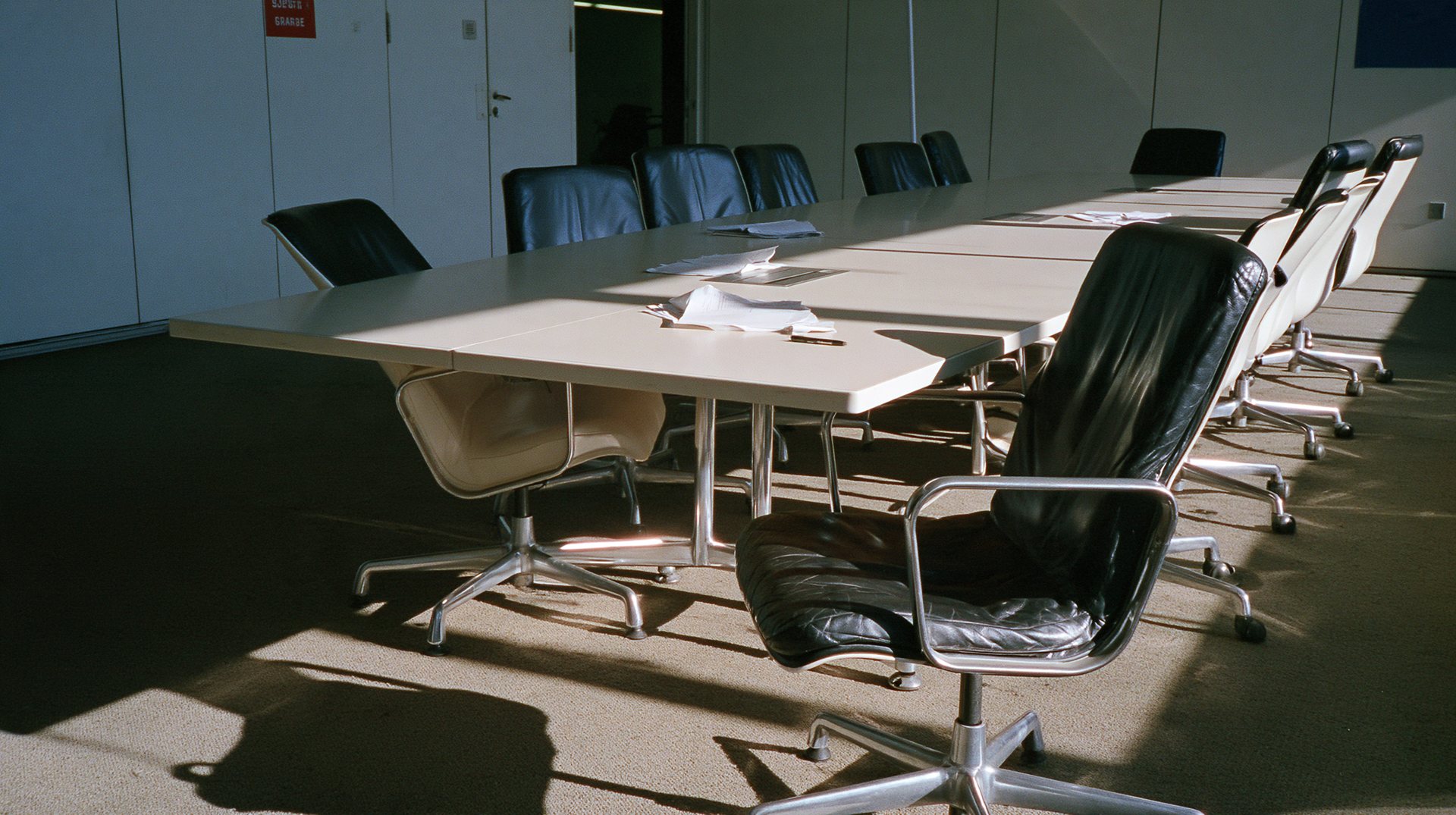 An empty boardroom with leather chairs and a long white table in low sun