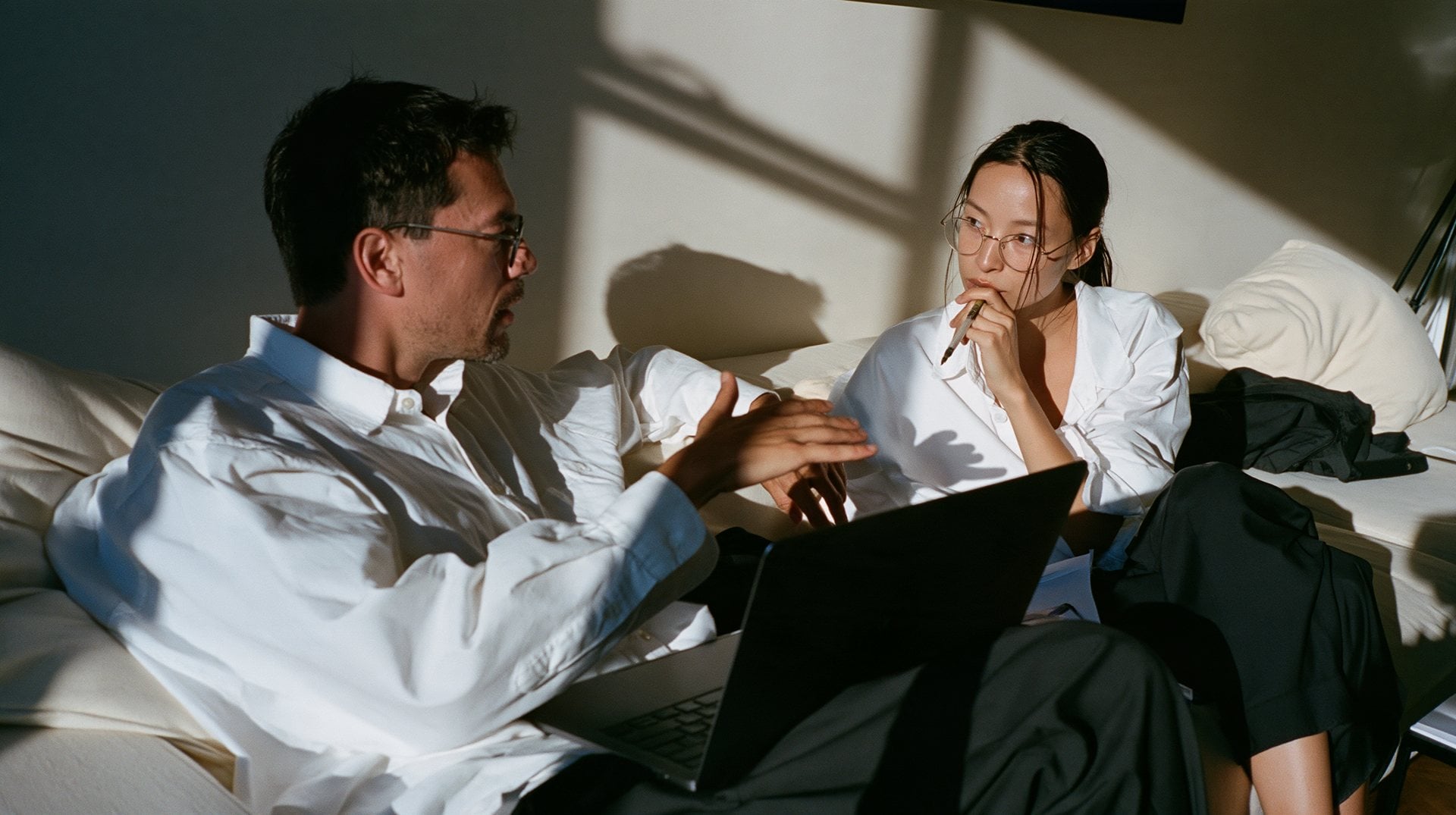 Two people talking through an idea on a sofa beside a laptop